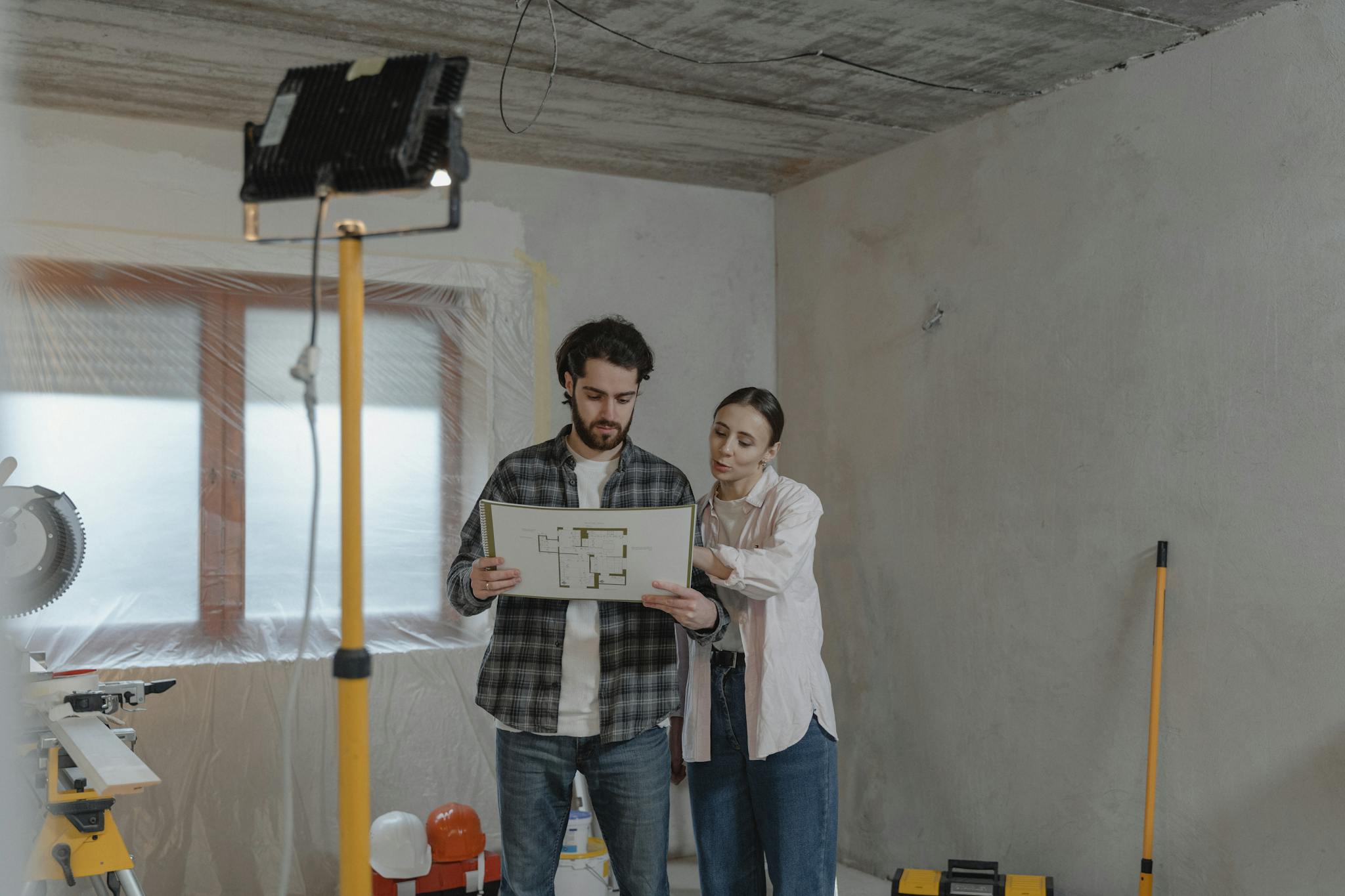 A couple examines blueprints in a partially renovated room, planning home improvements.